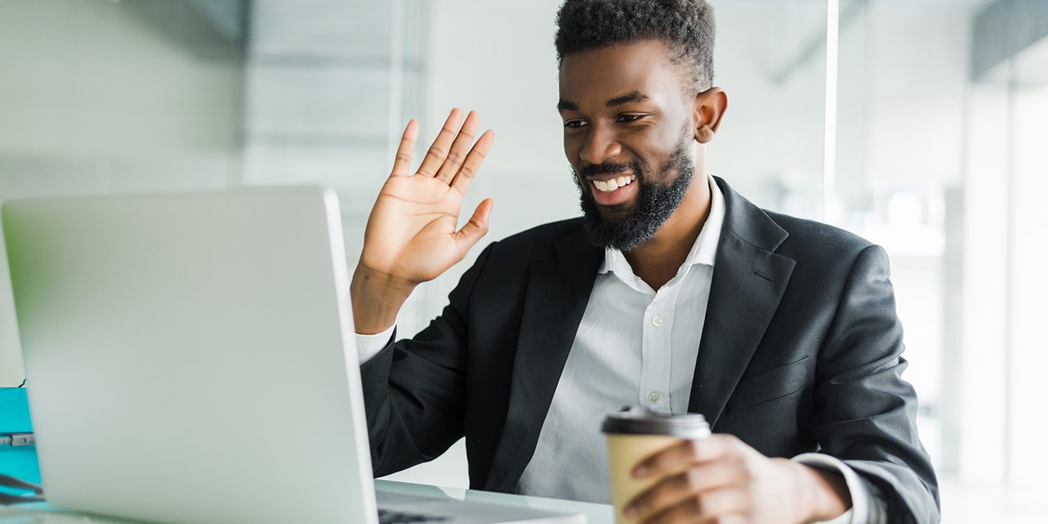 Young African manager with stubble sitting in front of open laptop wearing earphones while having video conference call with business partners